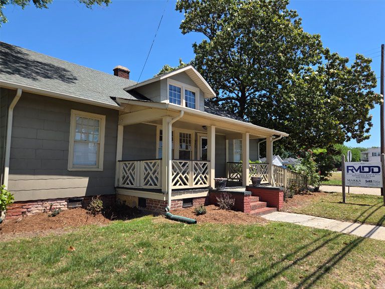 Charming cottage-style house with front porch, surrounded by greenery and a nearby real estate sign.