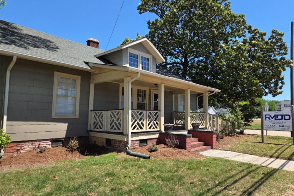 Charming cottage-style house with front porch, surrounded by greenery and a nearby real estate sign.