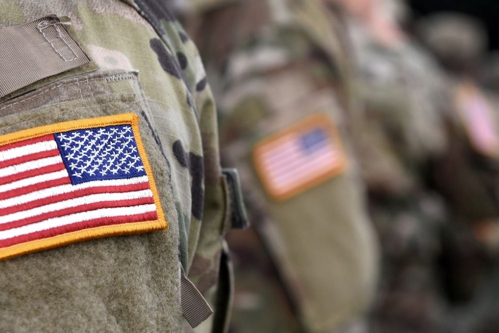 Close-up of a soldier's camouflage uniform with a U.S. flag patch, representing military service.