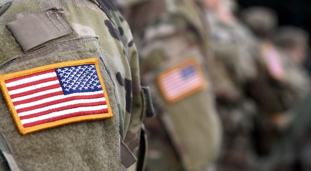 Close-up of a soldier's camouflage uniform with a U.S. flag patch, representing military service.