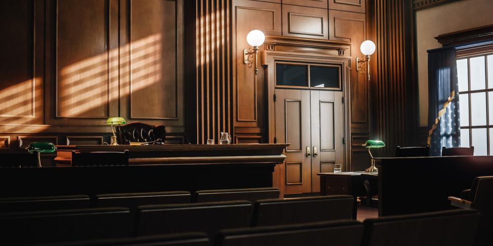 Elegant courtroom interior with wood paneling, empty seats, judge's bench, and warm sunlight streaming through windows.