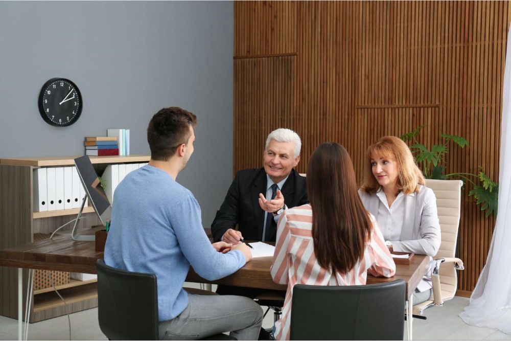 Business meeting with four people discussing in an office, using a laptop and documents on a wooden table.