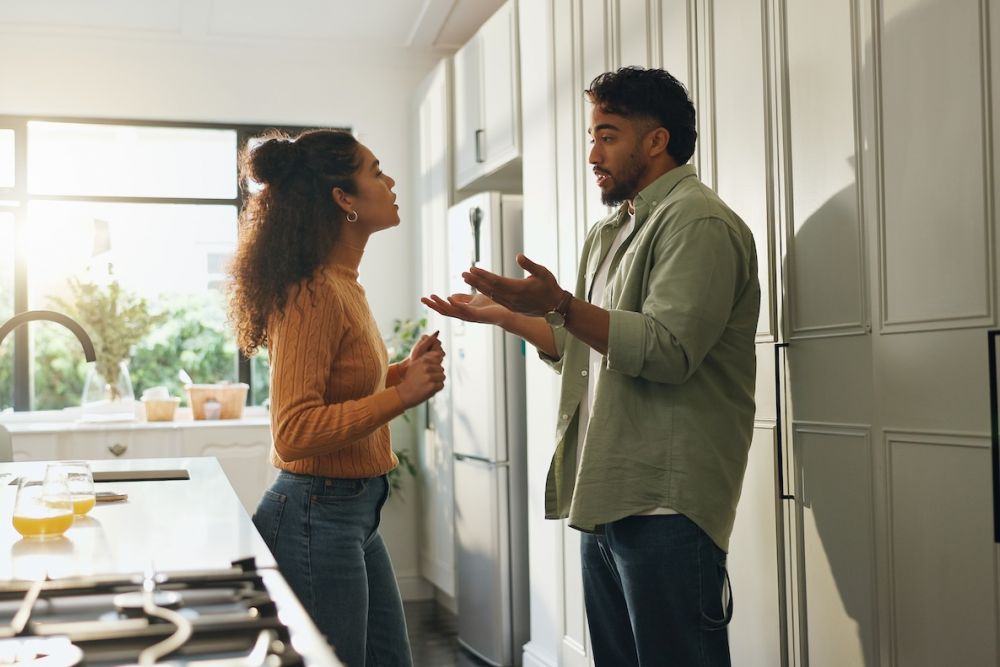 Couple having a spirited conversation in a bright kitchen with morning sunlight streaming through the window.