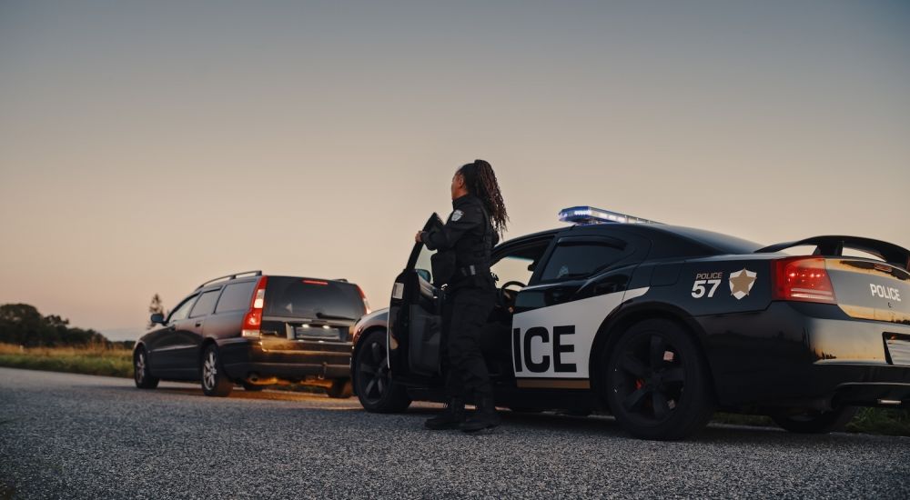 Police officer conducting a traffic stop at sunset with patrol car and vehicle on road.