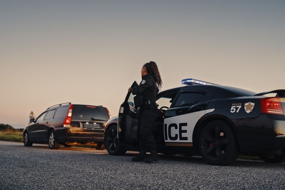 Police officer conducting a traffic stop at sunset with patrol car and vehicle on road.