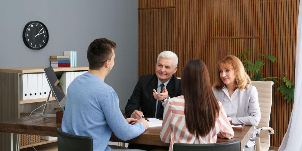 Business meeting with four people discussing in an office, using a laptop and documents on a wooden table.