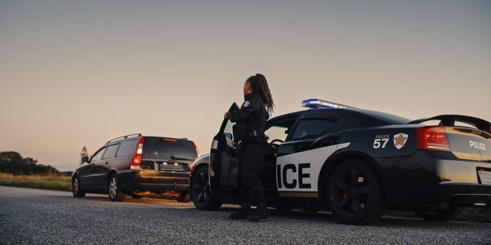 Police officer conducting a traffic stop at sunset with patrol car and vehicle on road.